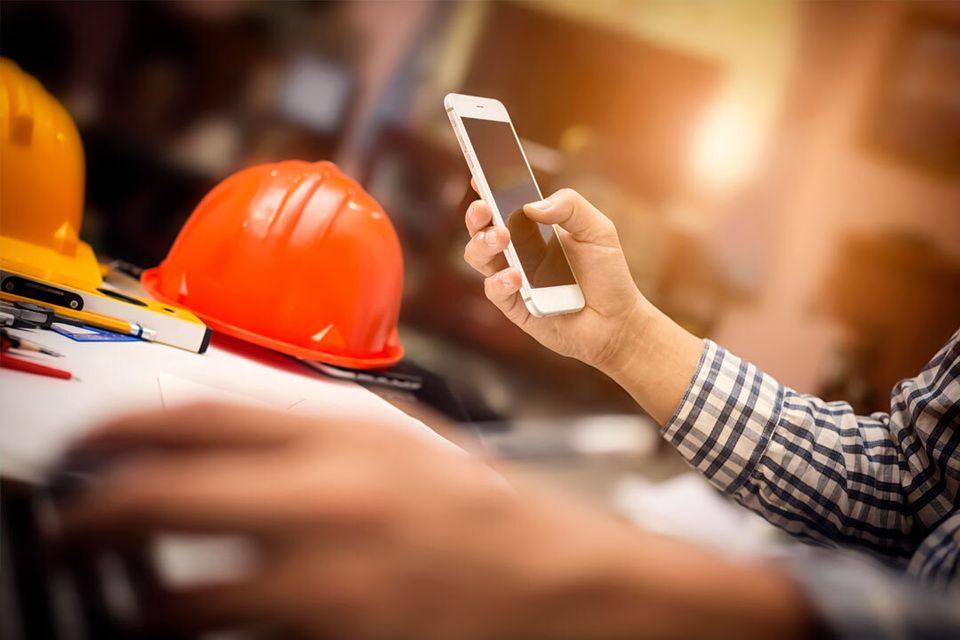 Construction company employee uses a smartphone to check business email at their desk.